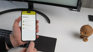 Modernes Arbeitsumfeld mit Smartphone in der Hand, das Benachrichtigungen auf einem Geschäfts-Dashboard zeigt, in einem Büro für digitales Marketing