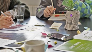 Kreatives Brainstorming mit Post-its und Marketingunterlagen auf einem Agenturtisch in Nordhorn, inklusive eines stilvollen Pflanzenkopfes und digitaler Hilfsmittel.
